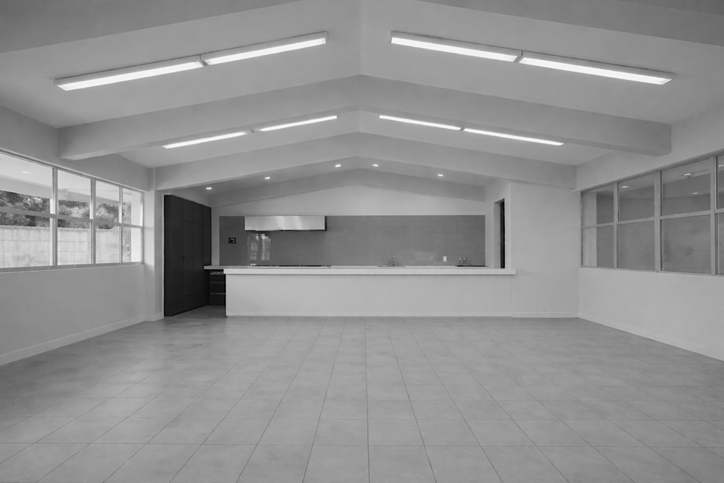 Interior de local comercial con acabados modernos, piso de loseta gris, techos altos con iluminación LED lineal y barra de servicio blanca, diseñado por M2 Arquitectos.
