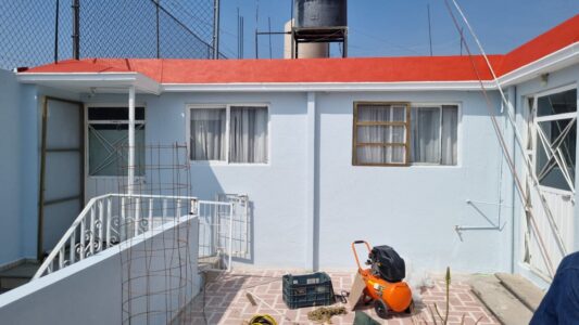 Detalle de mantenimiento residencial por M2 Arquitectos, mostrando el contraste entre la aplicación de pintura roja nueva en la cornisa y el tono azul claro original en los muros.