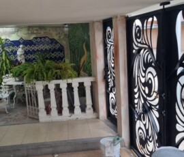 Proceso de remodelación de terraza residencial por M2 Arquitectos, mostrando una escalera de tijera, materiales de construcción y un portón de herrería negra con diseño artístico al fondo.