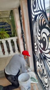 Técnico de M2 Arquitectos aplicando acabados de pintura y resanado en la base de una columna, junto a un portón de herrería artística en una obra residencial.