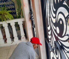 Técnico de M2 Arquitectos aplicando acabados de pintura y resanado en la base de una columna, junto a un portón de herrería artística en una obra residencial.