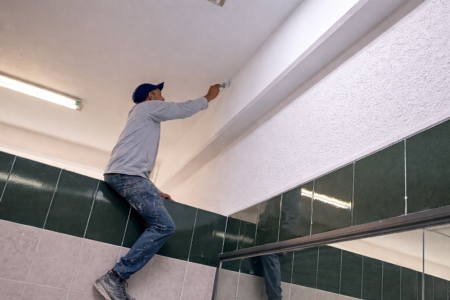 Técnico aplicando pintura en techo interior para acabado profesional en espacio comercial.