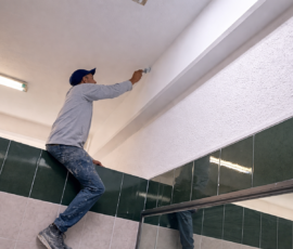 Técnico aplicando pintura en techo interior para acabado profesional en espacio comercial.