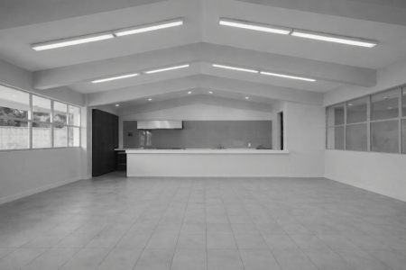 Interior de local comercial con acabados modernos, piso de loseta gris, techos altos con iluminación LED lineal y barra de servicio blanca, diseñado por M2 Arquitectos.