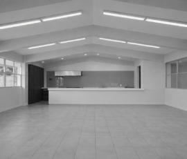 Interior de local comercial con acabados modernos, piso de loseta gris, techos altos con iluminación LED lineal y barra de servicio blanca, diseñado por M2 Arquitectos.