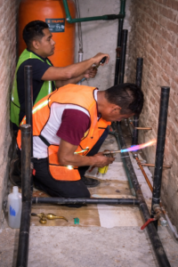 Dos técnicos realizando trabajos de fontanería, utilizando un soplete para soldar tuberías de cobre en una instalación de construcción.