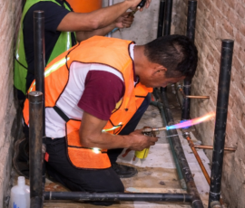 Dos técnicos realizando trabajos de fontanería, utilizando un soplete para soldar tuberías de cobre en una instalación de construcción.